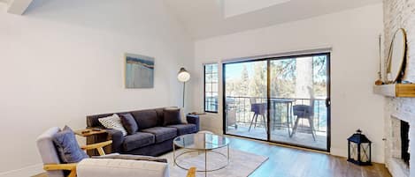 A spacious living room with a high ceiling, a large sliding glass door leading to an outdoor area, a fireplace, and a modern light fixture.