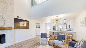 A spacious living room with a fireplace, a dining area with wooden chairs, and a kitchen in the background. - Lake Arrowhead Views! Condo w/ Shared Pool & Spa (Lake Arrowhead)