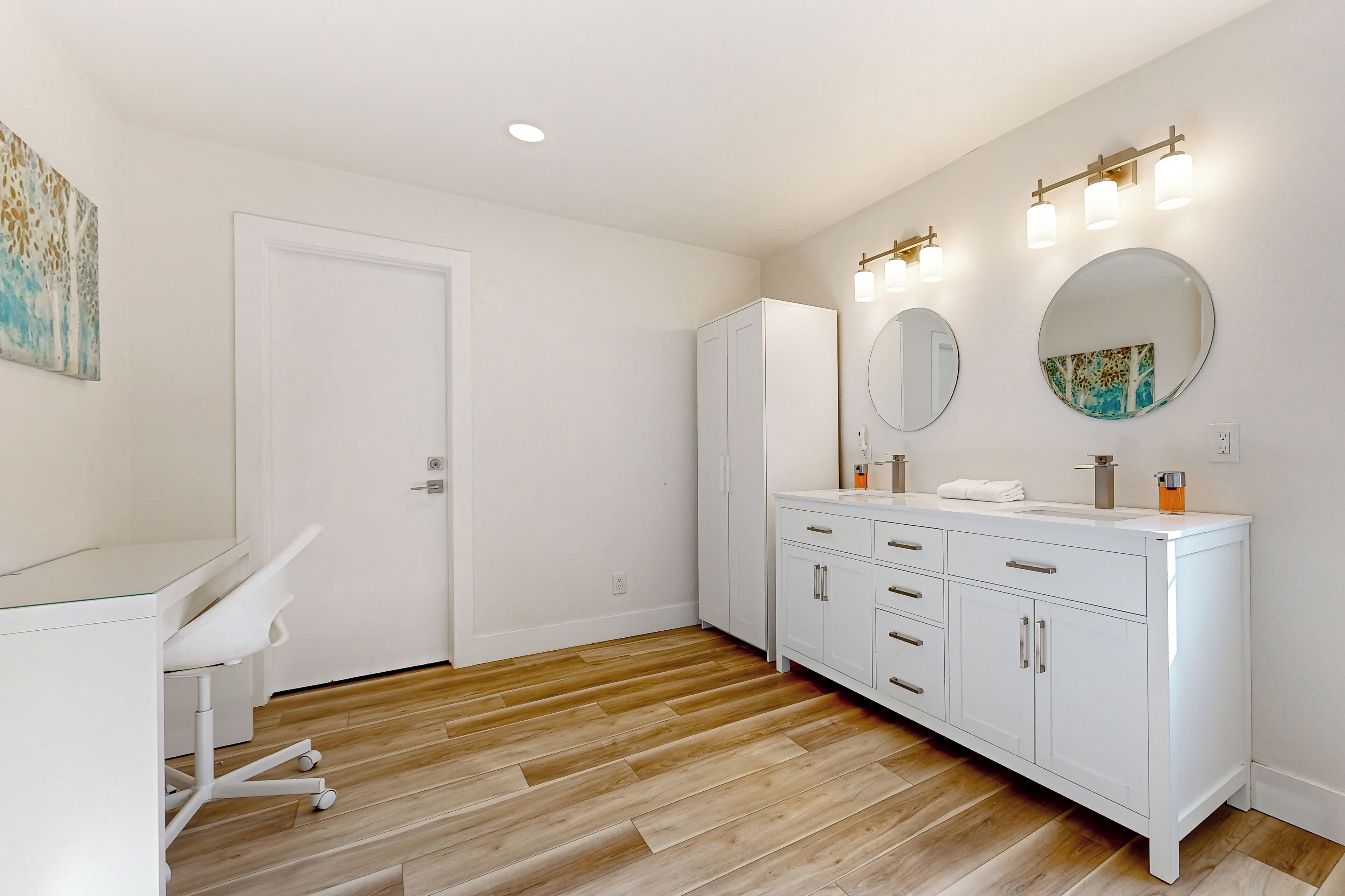 Une salle de bain moderne avec des meubles blancs, deux miroirs et un plancher en bois.