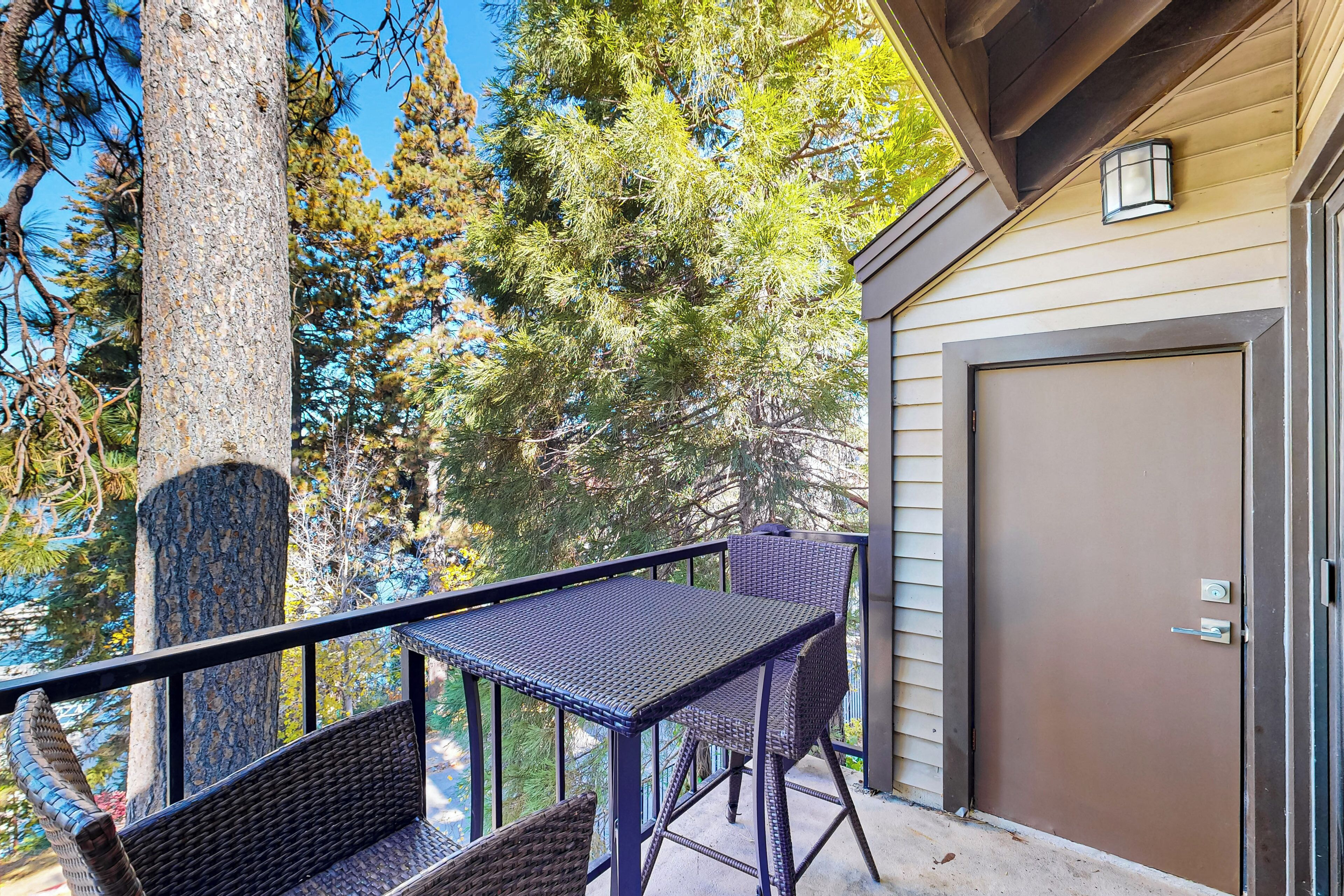 A balcony with wicker furniture, a door, and a view of trees.