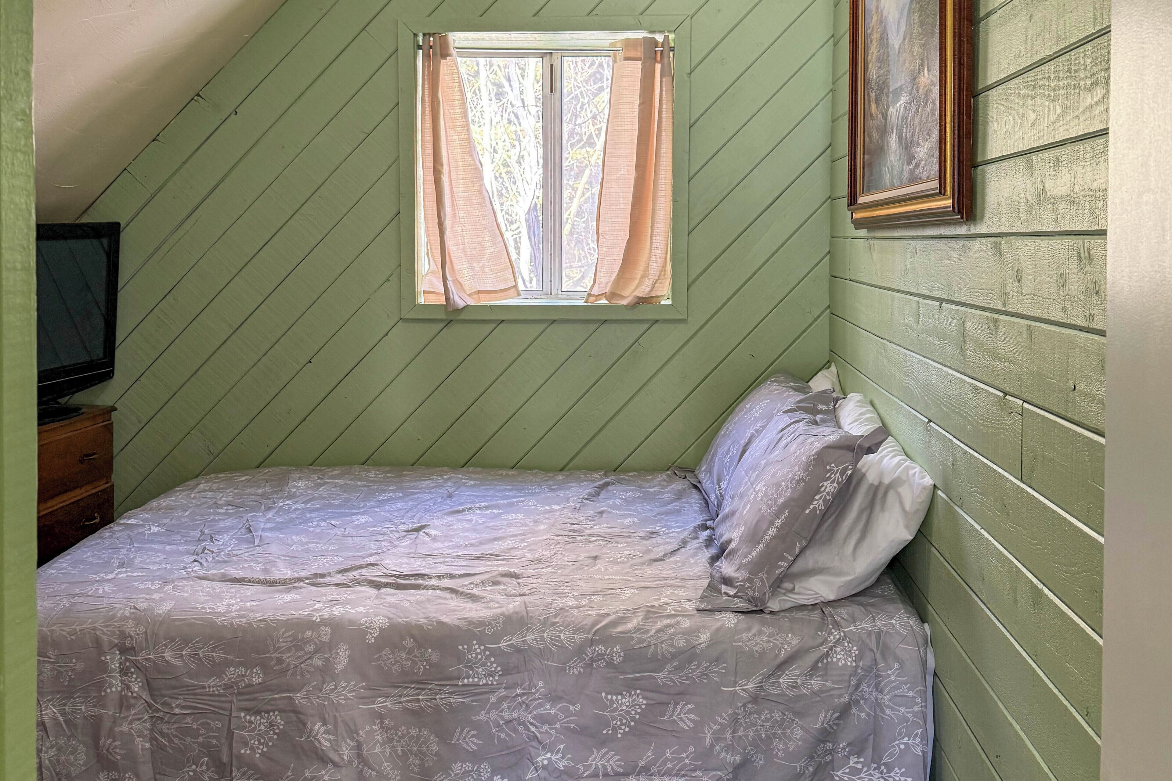 Een slaapkamer met een bed, een raam met gordijnen, een dressoir en een schilderij aan de muur.