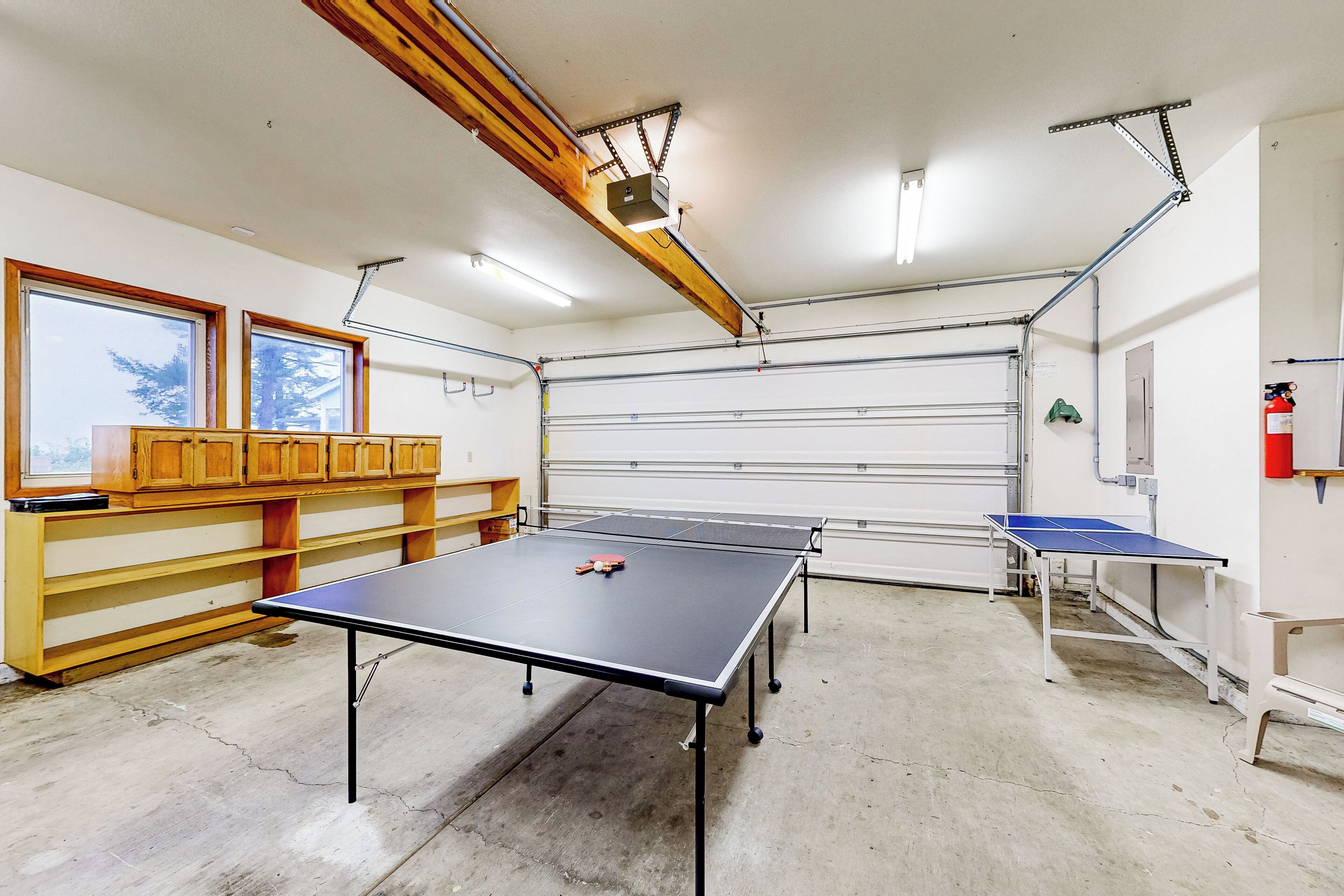 Amplio espacio interior con mesas de ping pong, armarios de madera y una puerta de garaje.