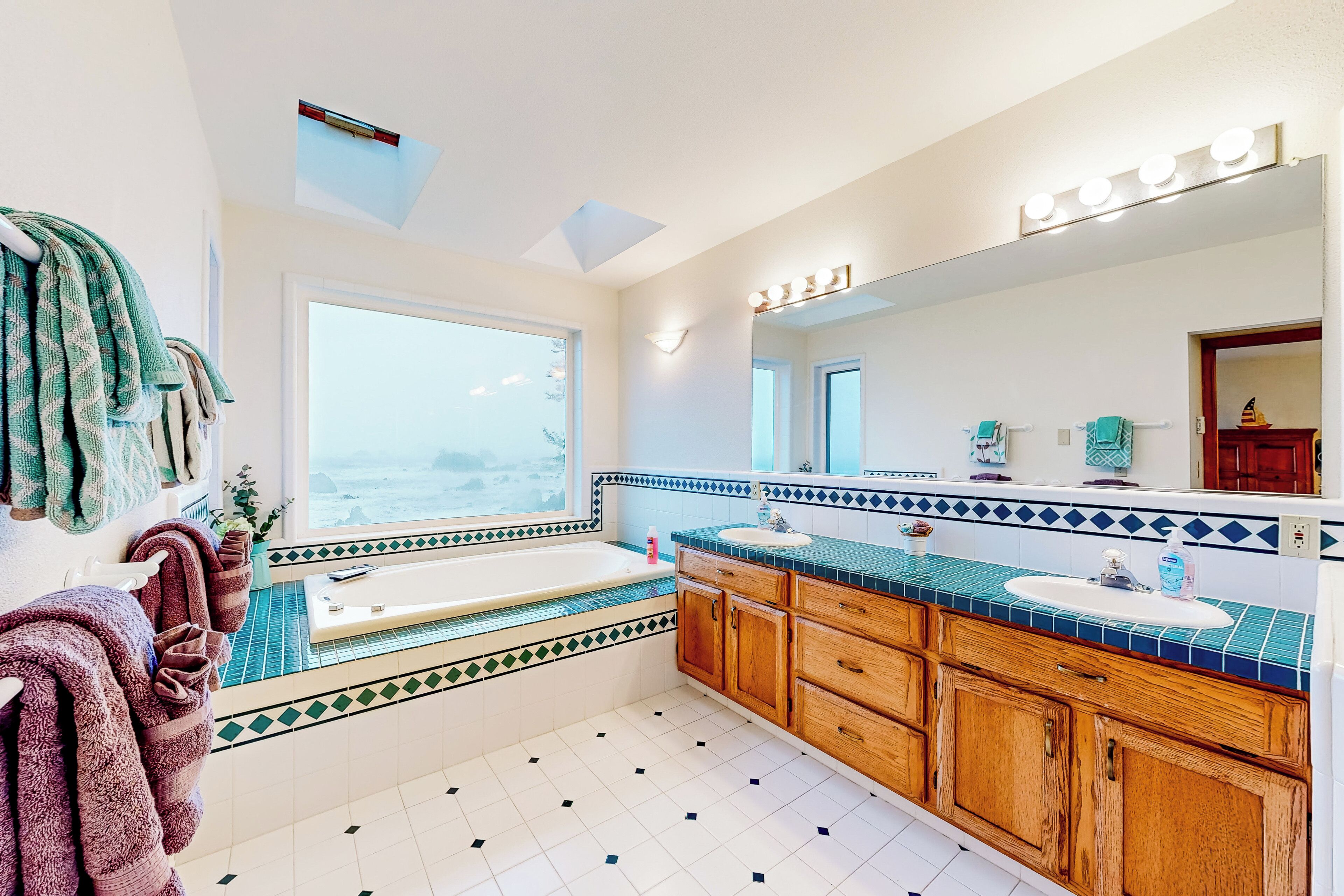 Ein Badezimmer mit großem Fenster, einer Badewanne, einem Waschbecken und Holzschränken.