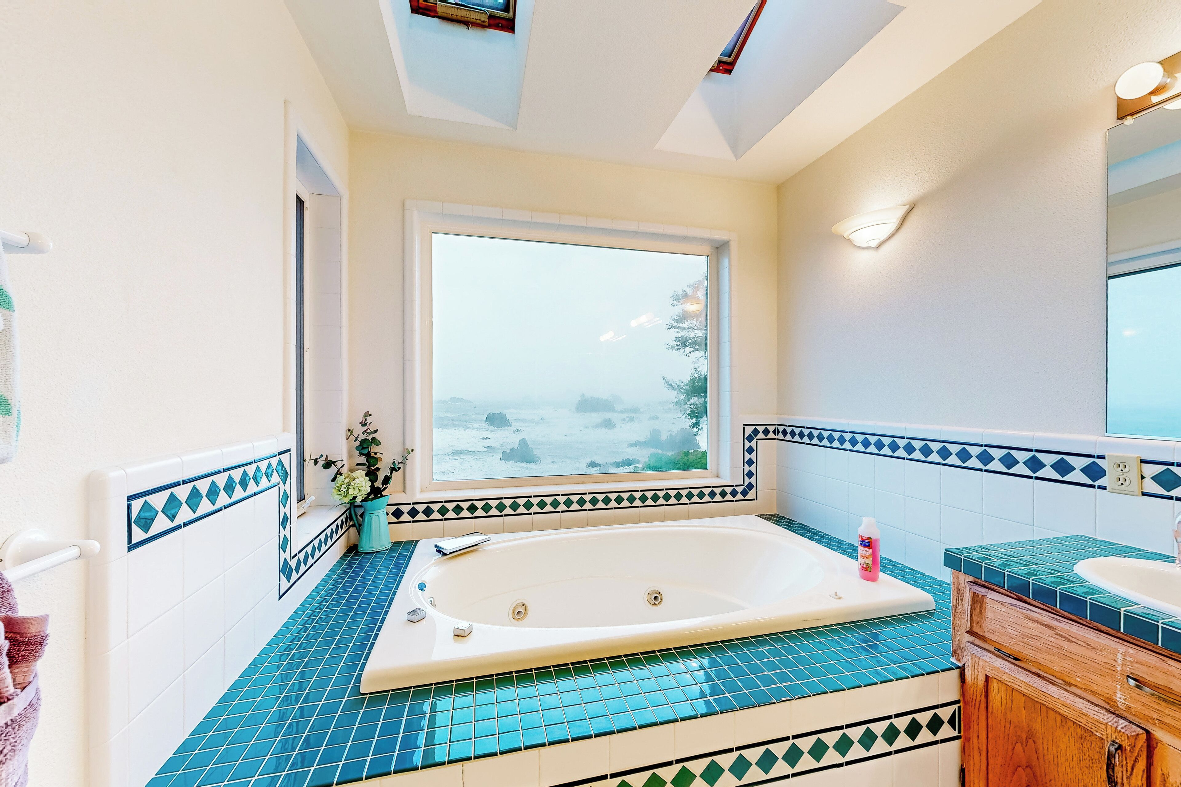 A bathroom with a large bathtub, a window with a view of the sea, and a tiled floor.