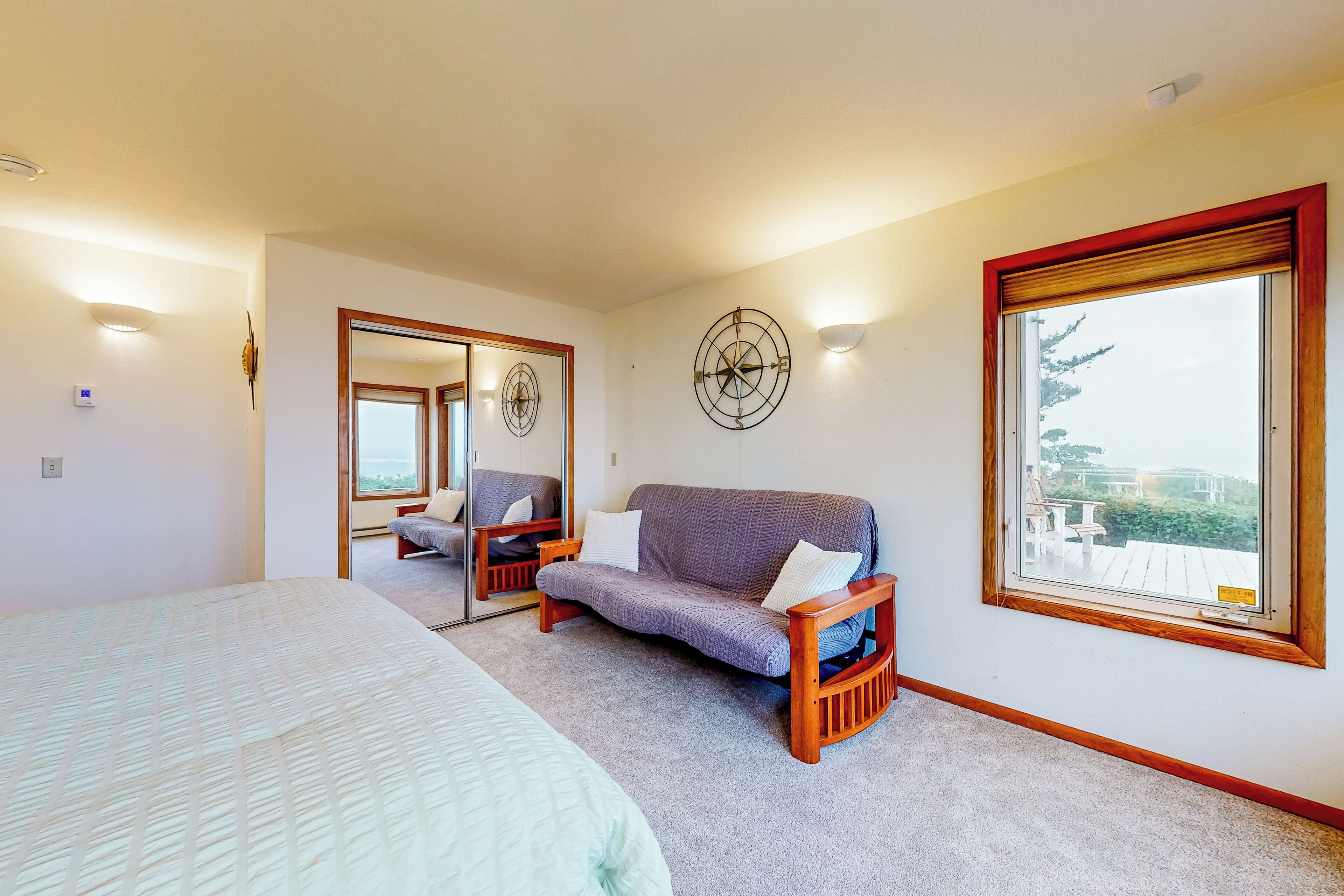 A bedroom with a large bed, a sofa, a chair, a window with a view, and a wall clock.
