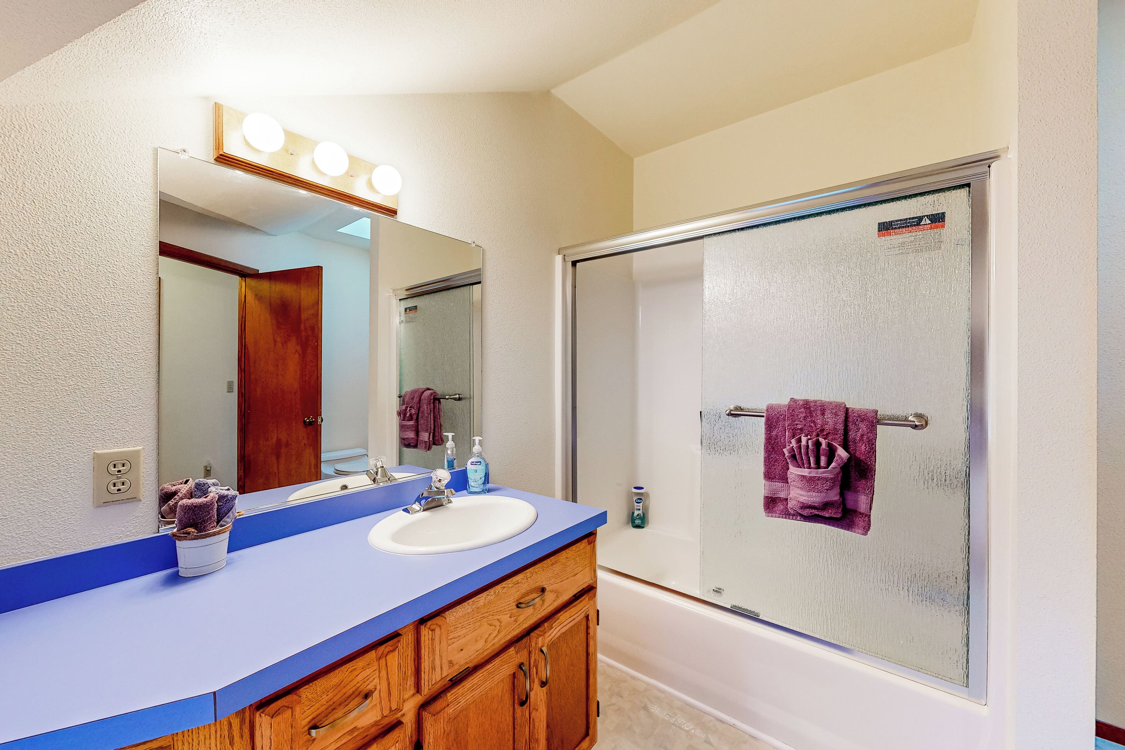A bathroom with a blue vanity, a white sink, a mirror with lights, a glass shower enclosure, and a wooden cabinet.