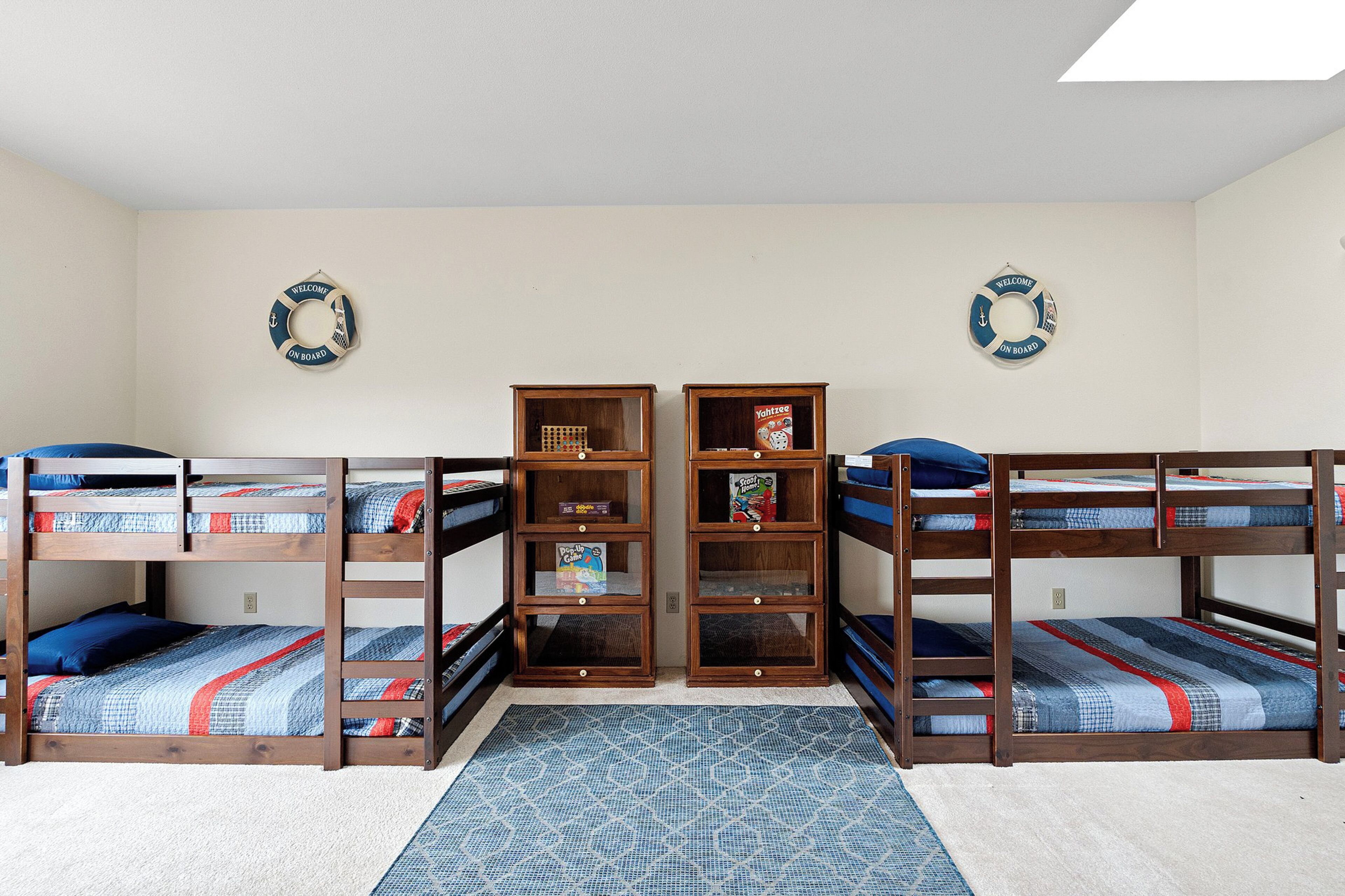 A bunk bed room with two bunk beds, a bookshelf, and two welcome wreaths on the walls.