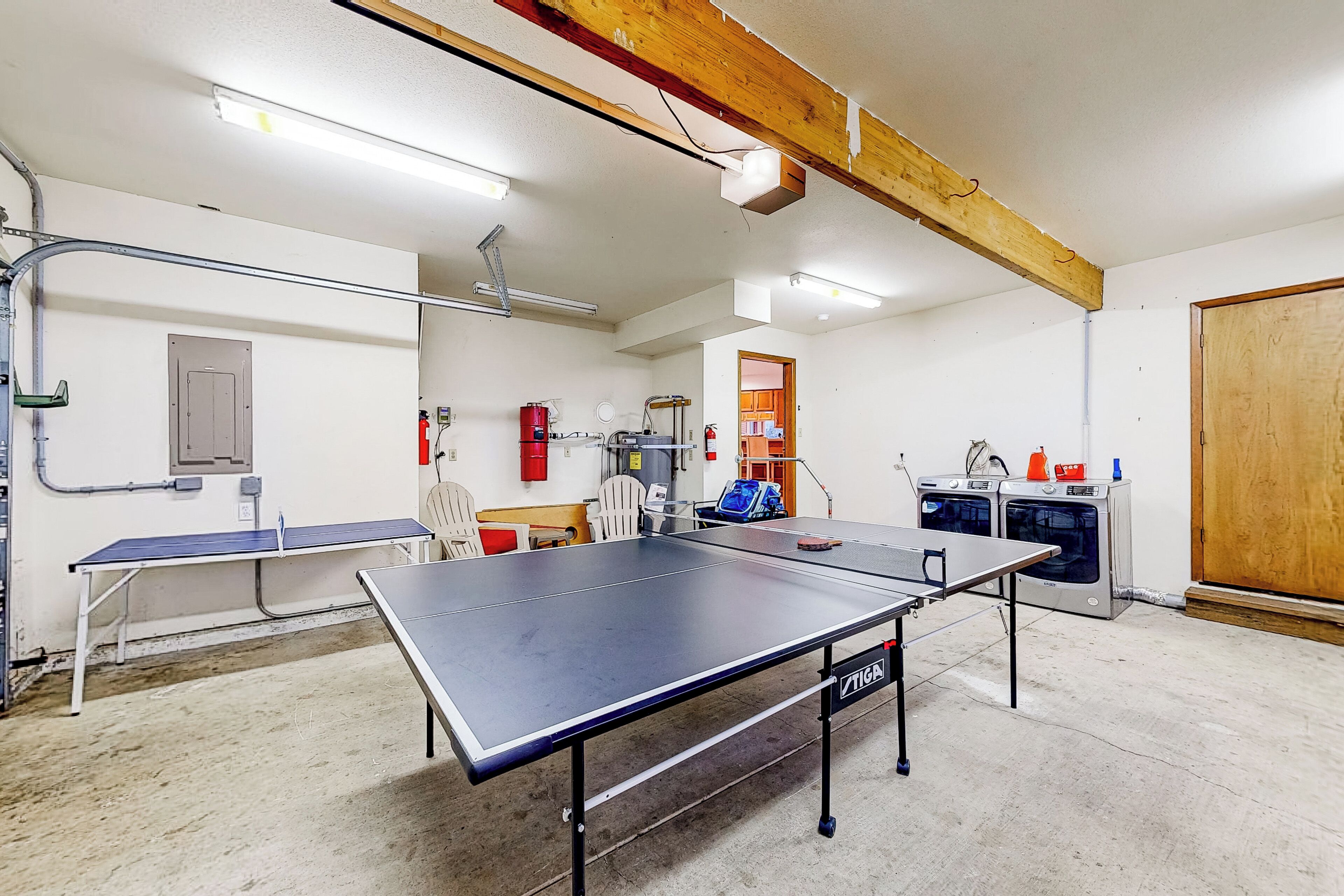 A room with a ping pong table, a washing machine, and a fire extinguisher.