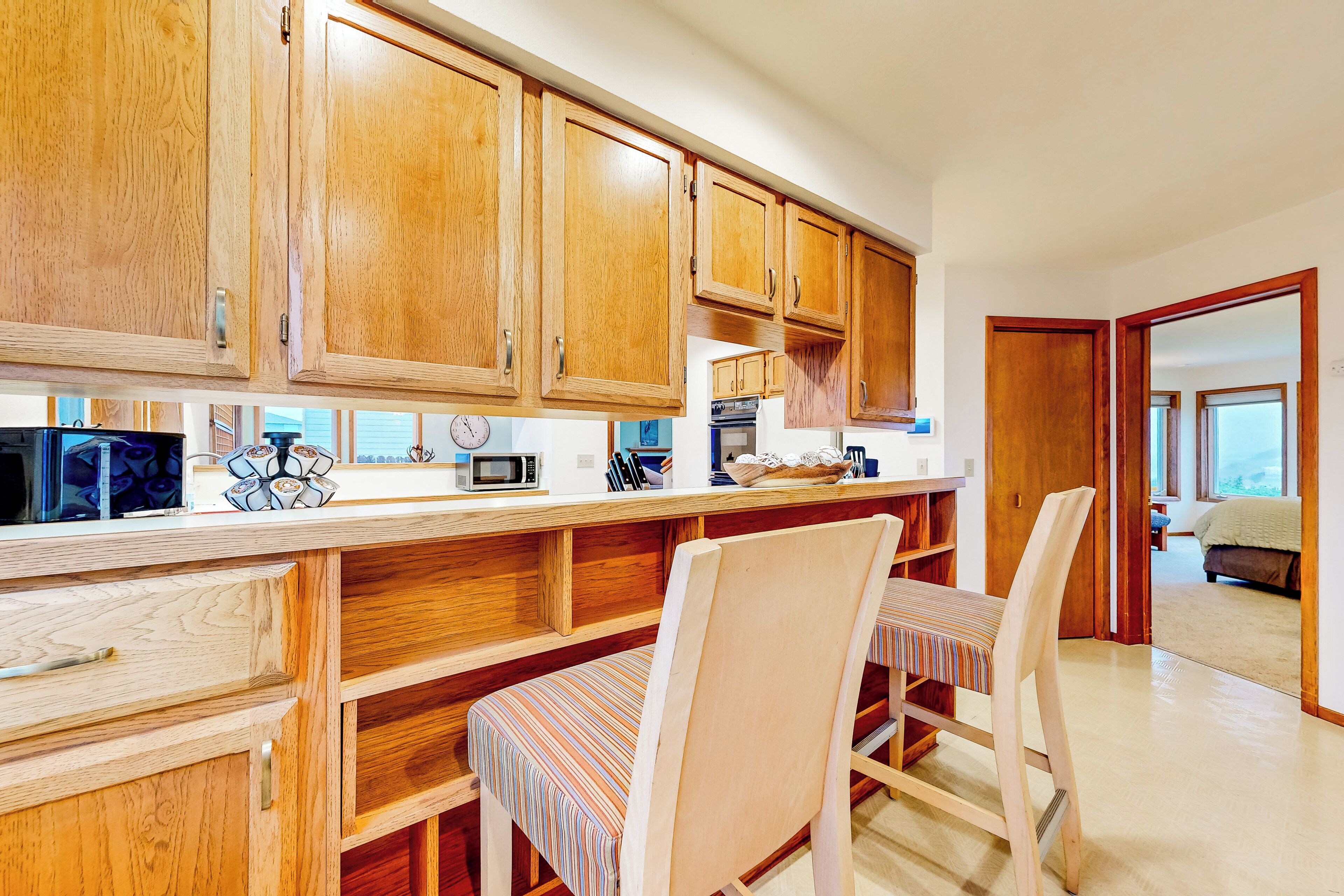 Una cocina con armarios de madera, microondas y comedor con sillas a rayas.