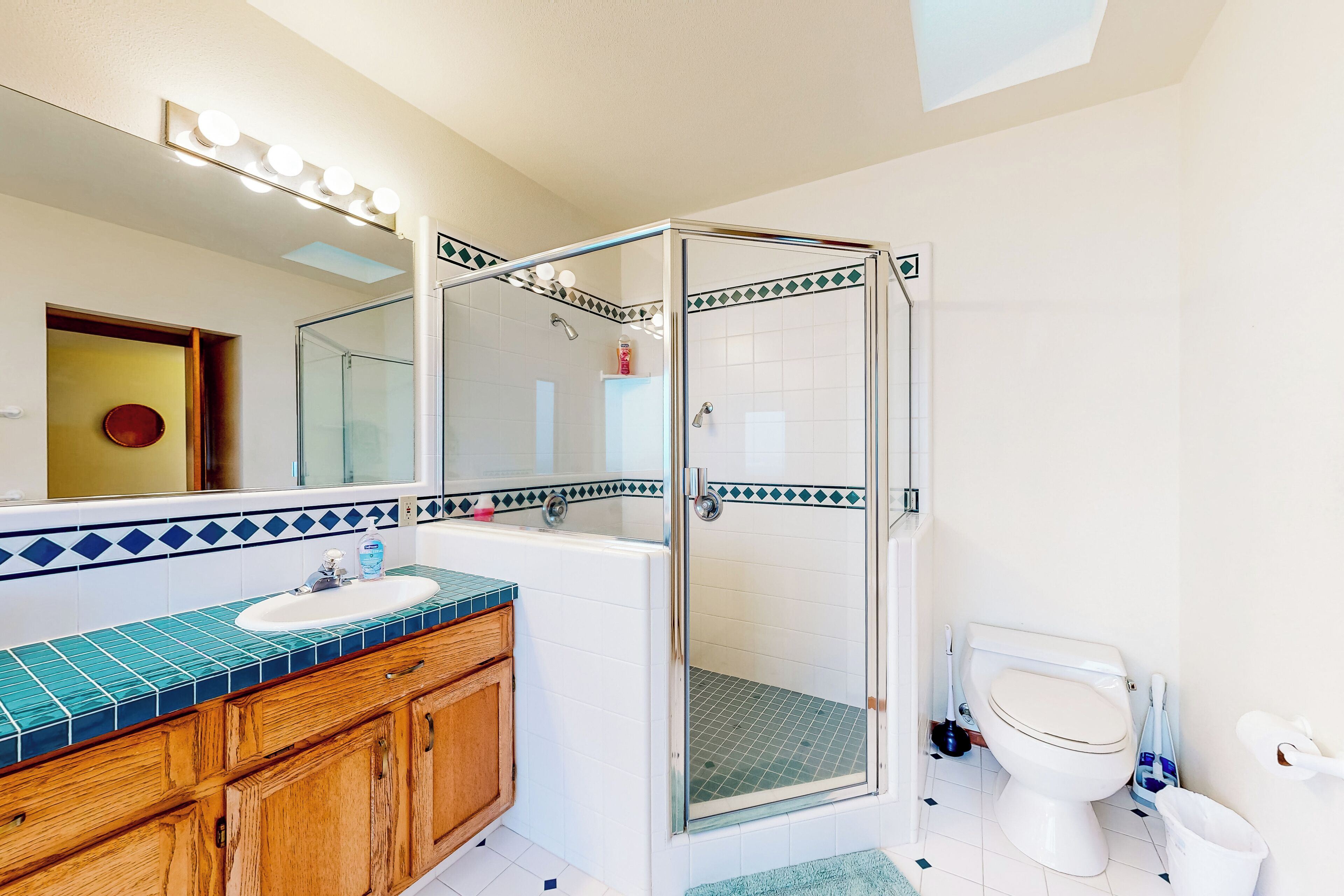 A bathroom with a glass-enclosed shower, a sink with a blue-tiled countertop, and a toilet.