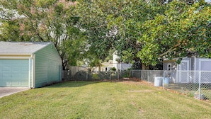 A fenced backyard with a green shed, a white garage, and a tree with pink blossoms. - 8 Mi to Dtwn New Orleans! Newly Renovated Home (Metairie)
