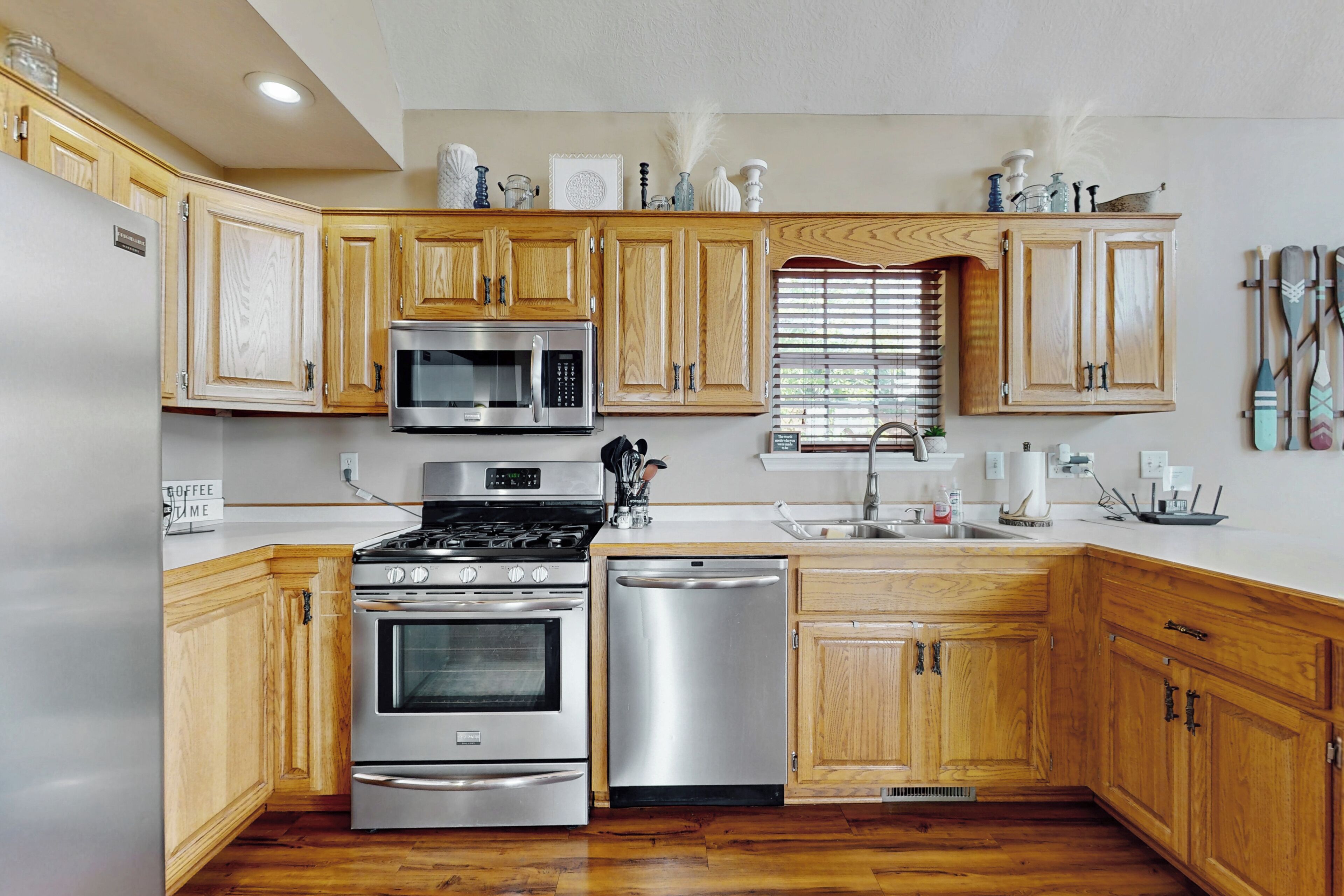 A modern kitchen with wooden cabinets, stainless steel appliances, and a window with blinds.