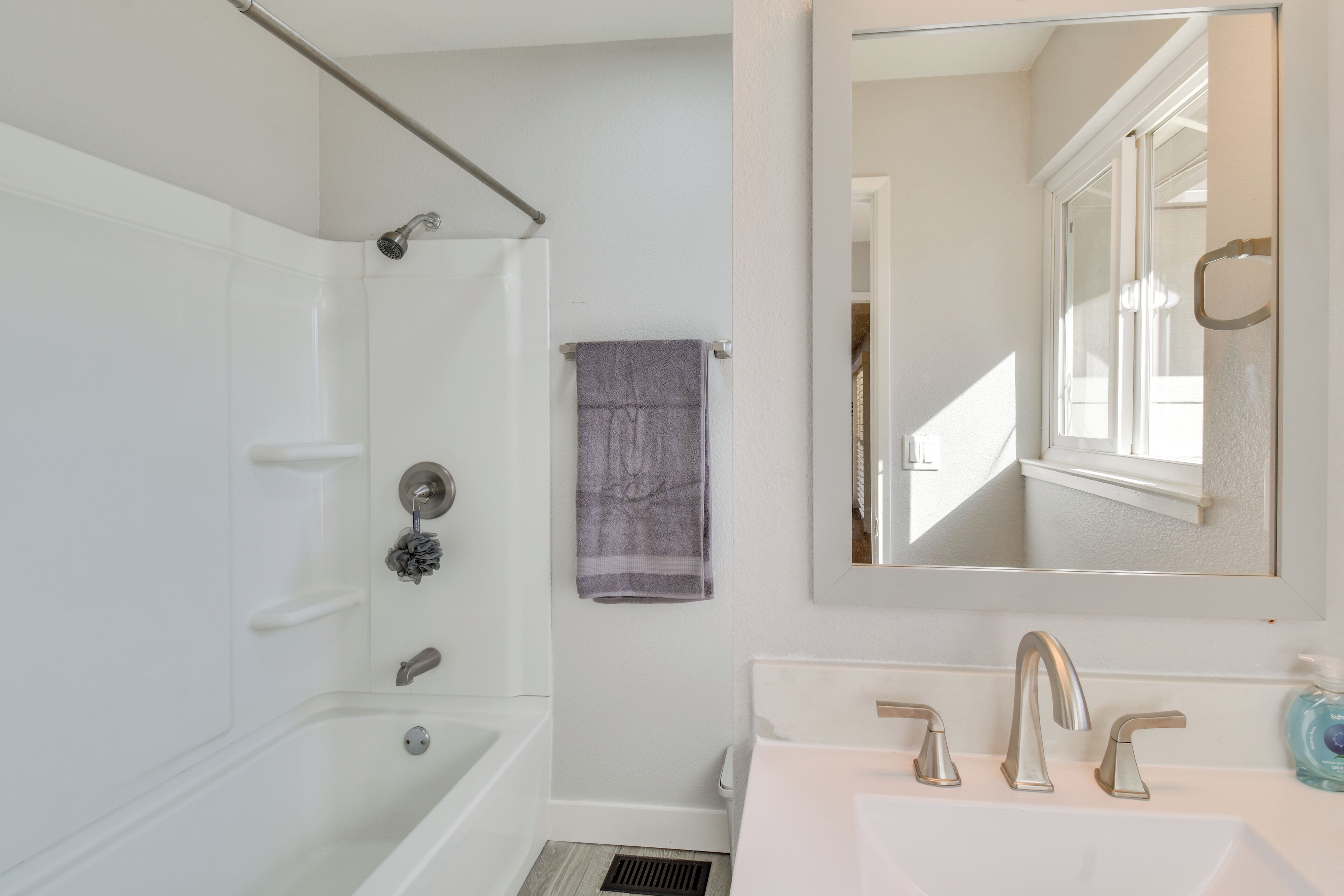 A bathroom with a bathtub, a sink with two faucets, and a towel hanging on the wall.
