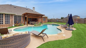 Ein Garten mit Swimmingpool, Gartenmöbeln und einer überdachten Terrasse.
