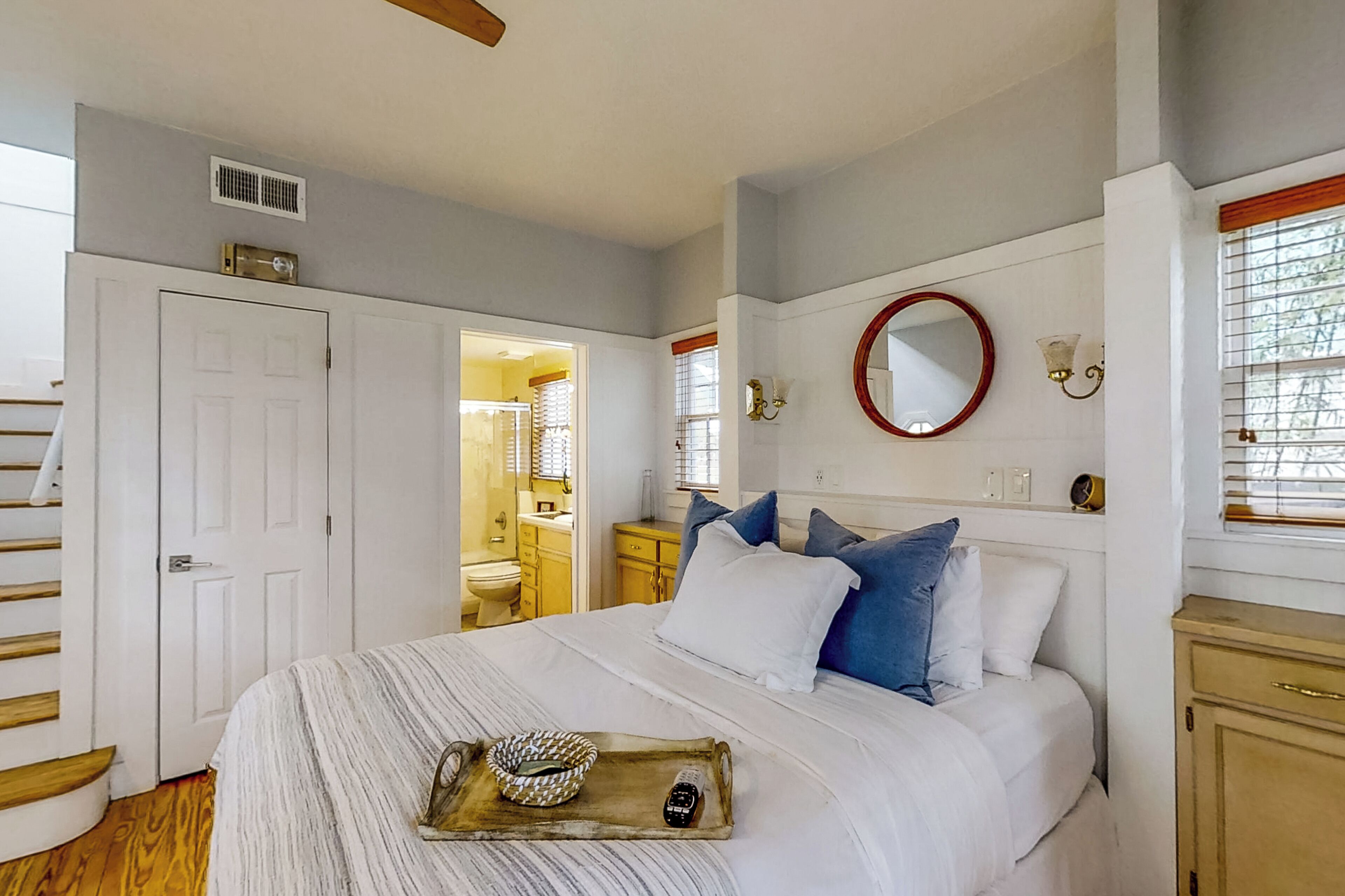 A bedroom with a bed, a bedside table, a mirror, and a window with blinds.
