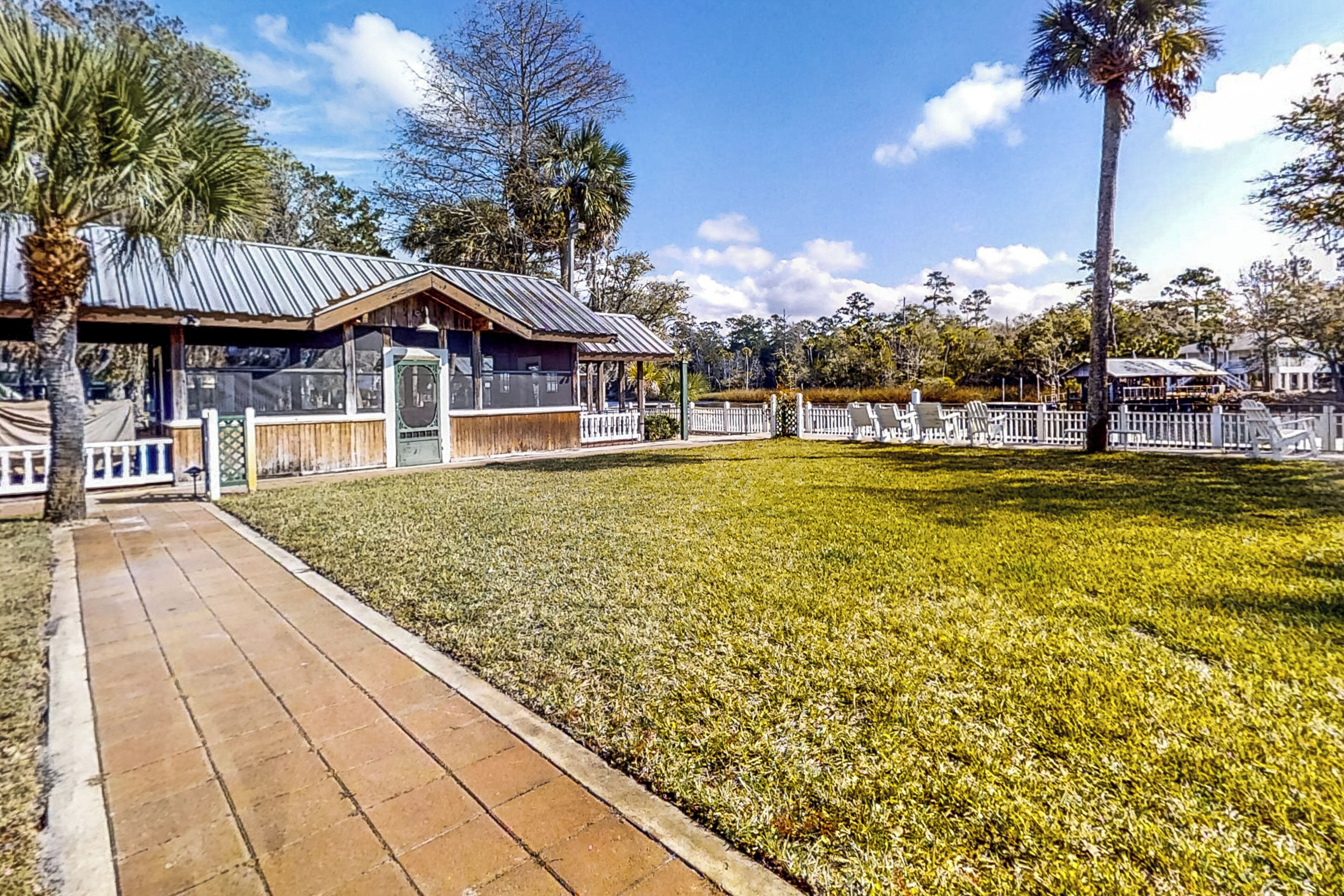 A well-maintained grassy area with a paved walkway, a covered seating area, and a white fence.
