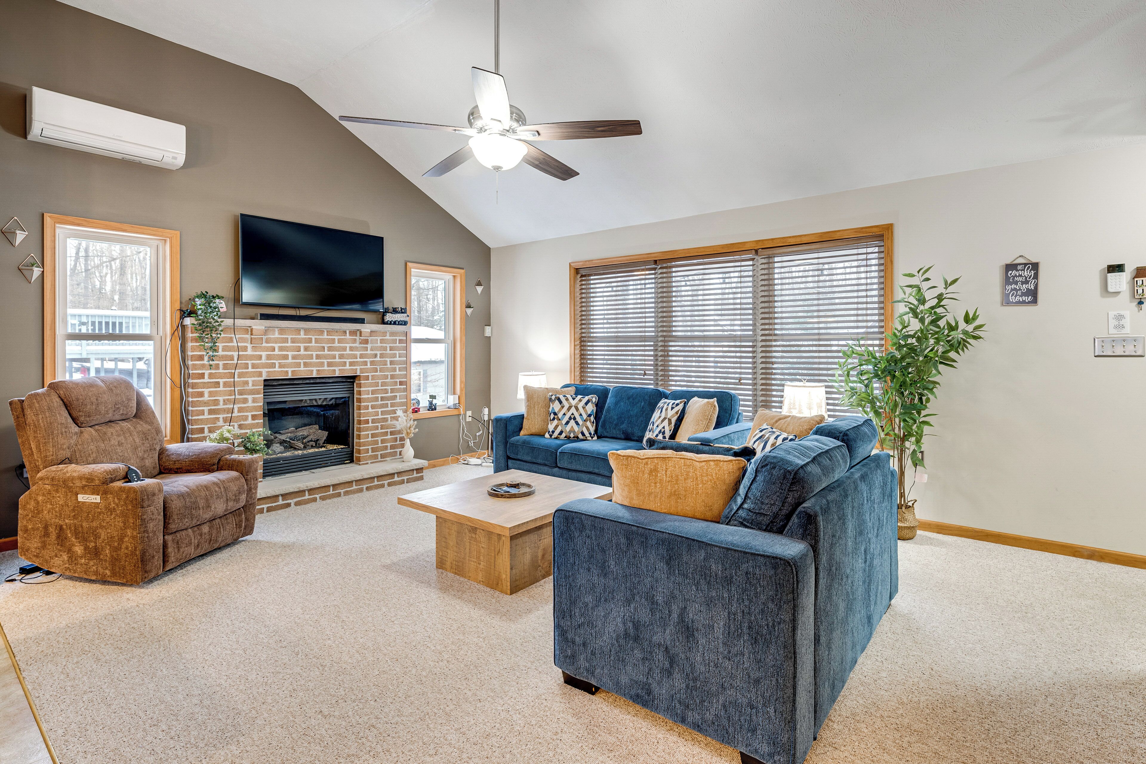 A living room with a fireplace, a blue sofa, a recliner, and a ceiling fan.