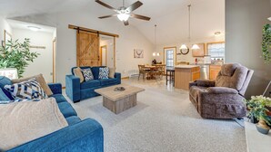 A spacious living room with a blue sofa, a brown recliner, and a wooden coffee table. A ceiling fan and a kitchen area are visible in the background. - Arrowhead Lake Community Perks! Cozy Family Home (Pocono Lake)
