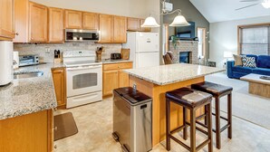A modern kitchen with granite countertops, wooden cabinets, stainless steel appliances, and a central island with bar stools. - Arrowhead Lake Community Perks! Cozy Family Home (Pocono Lake)