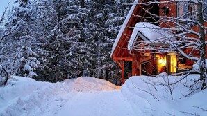 A wooden cabin with a warm interior light, surrounded by snow-covered trees and a snow-covered ground. - Secluded Mtn Retreat w/ Resort Perks in Whitefish! (Whitefish)