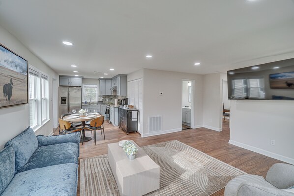 A modern living room with a blue sofa, a coffee table, and a dining area with a table and chairs. - Walk to Leesburg Historic District: Family Retreat (Leesburg)