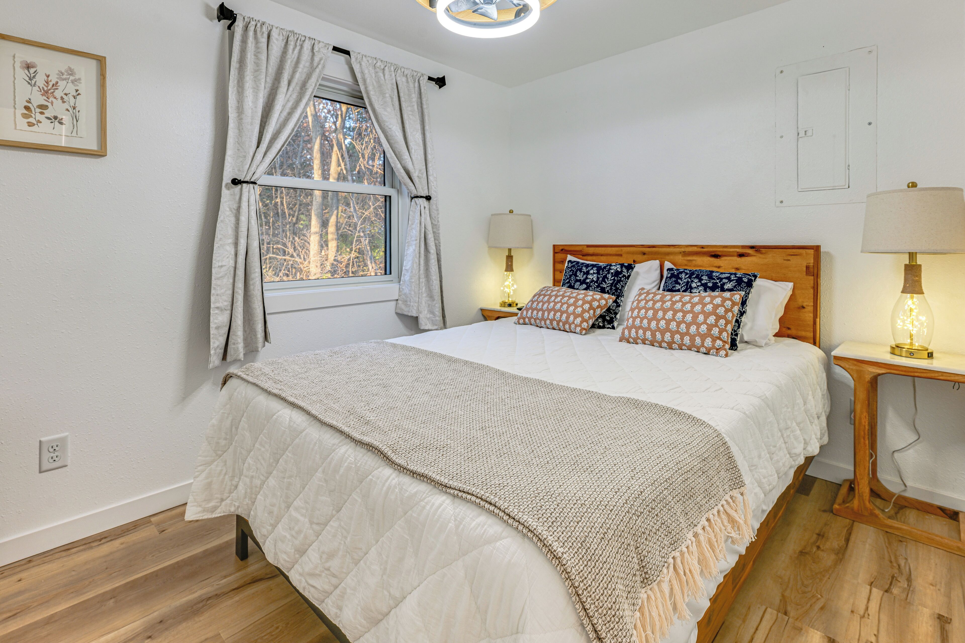 Une chambre à coucher avec un grand lit, deux lampes de chevet, une fenêtre avec des rideaux et une tête de lit en bois.