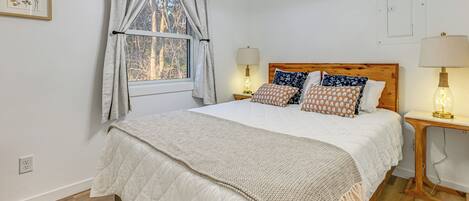 A bedroom with a large bed, two bedside lamps, a window with curtains, and a wooden headboard.