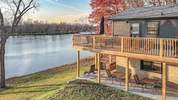 A house with a deck overlooking a lake, featuring outdoor seating and a covered area. - Riverfront Reset! Dells Cabin w/ Kayaks & Deck (Wisconsin Dells)