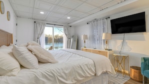 A bedroom with a large bed, a TV mounted on the wall, a bedside table with a lamp, and a view of a lake through the window. - Riverfront Reset! Dells Cabin w/ Kayaks & Deck (Wisconsin Dells)
