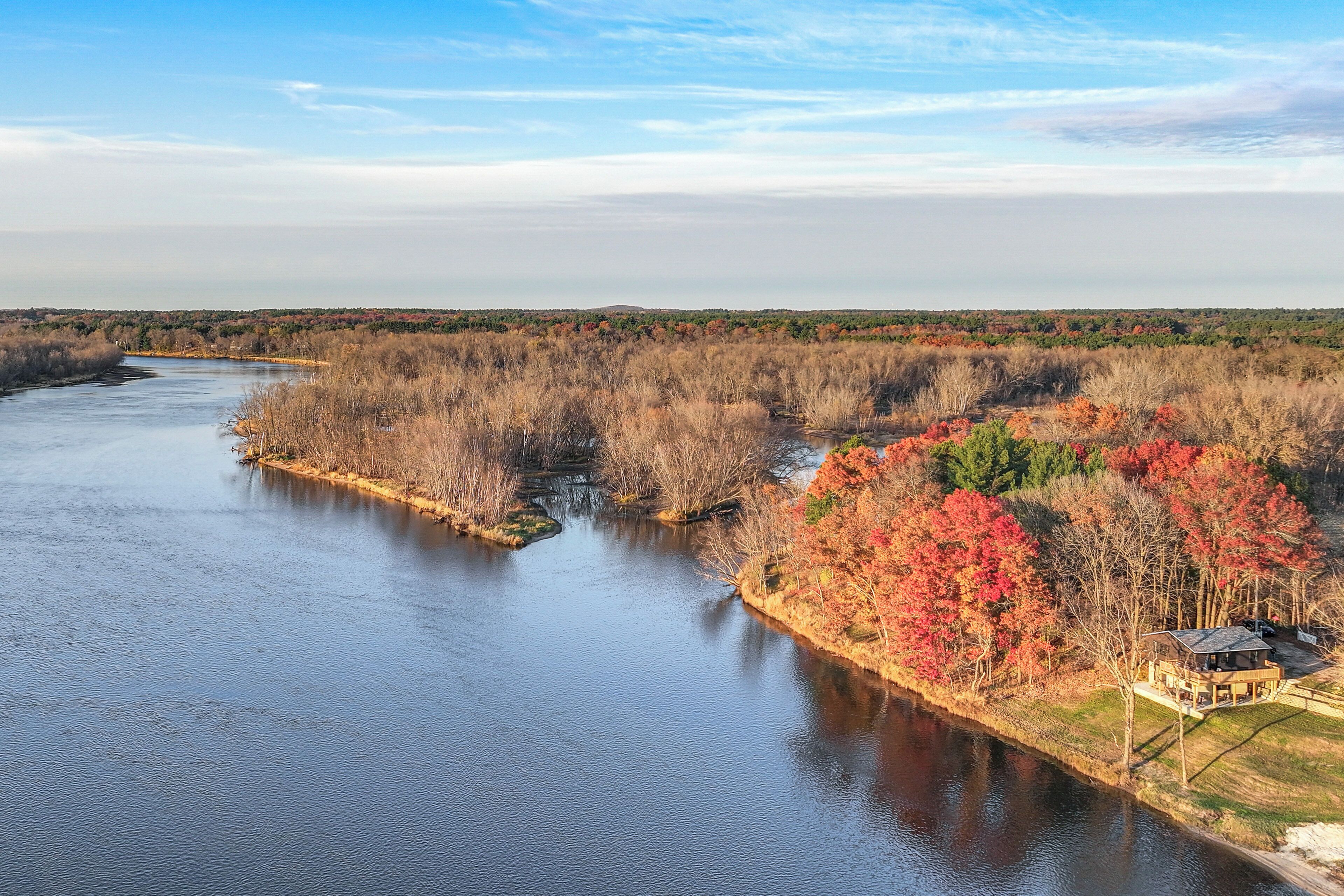 A river with a house on the right bank, surrounded by autumn foliage.