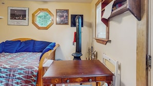 A bedroom with a bed, a wooden dresser, a heater, and framed pictures on the wall. - Tiny House at Sugarbush North: Adventure Hub! (Waitsfield)