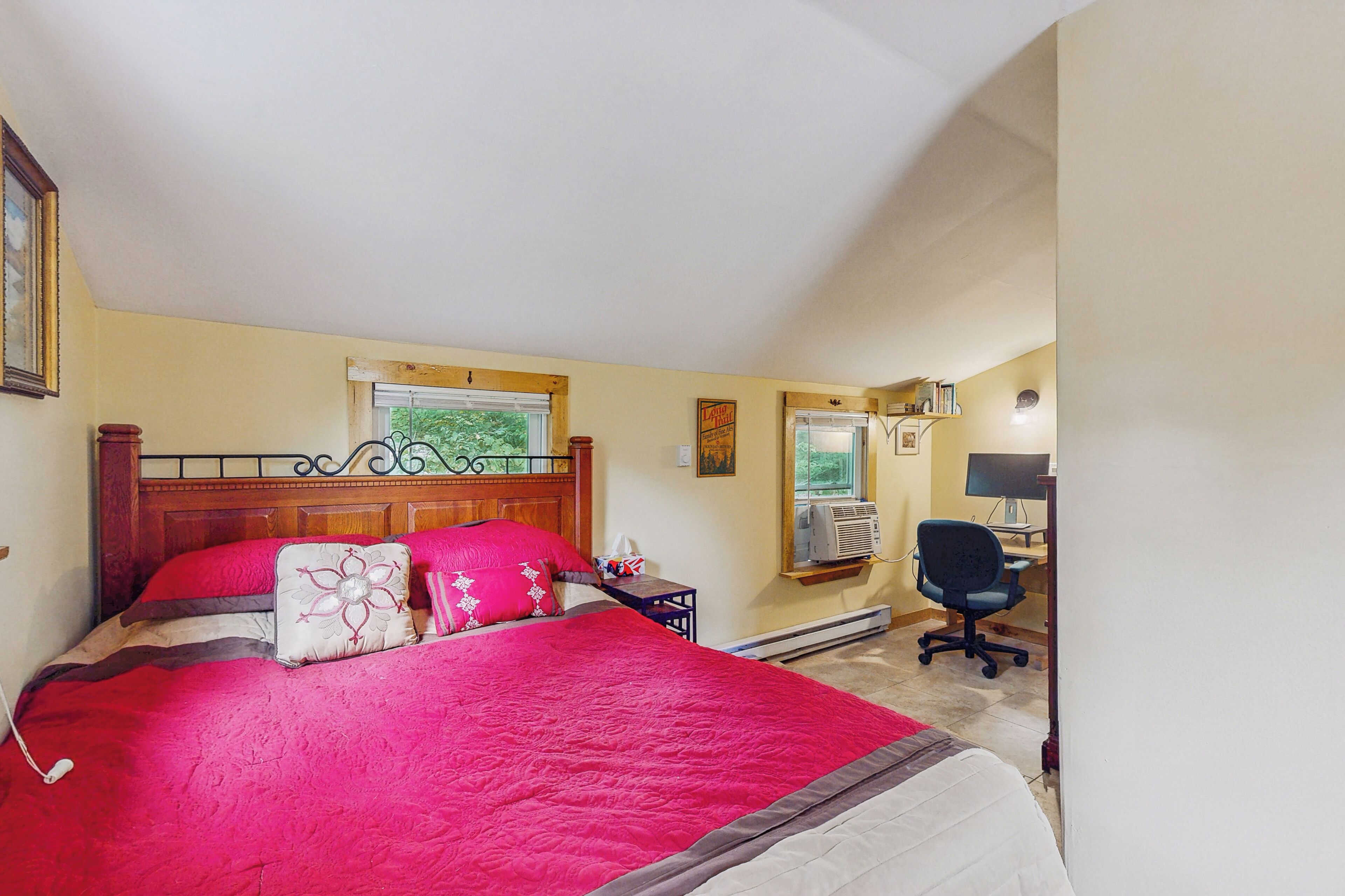 A bedroom with a large bed, a wooden headboard, a desk with a computer, and a window with blinds.