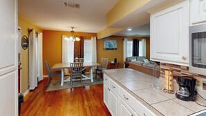 Cocina compacta con armarios blancos, comedor con mesa y sillas, y sala de estar con sofá y televisor.