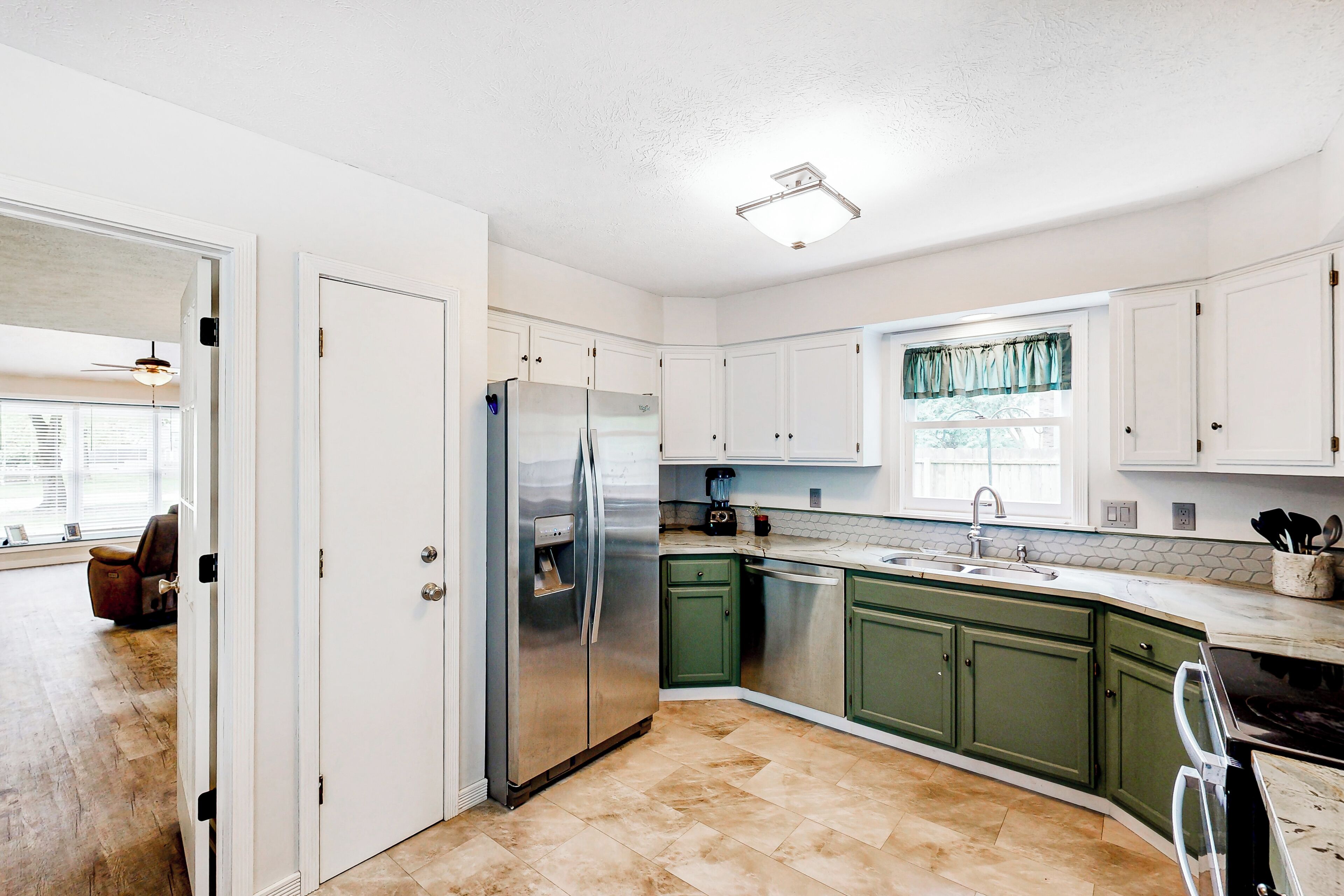 A kitchen with white cabinets, a stainless steel refrigerator, and a window with curtains.