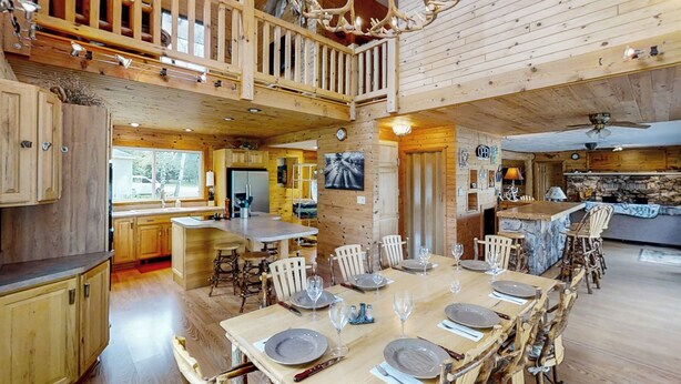 Una cabaña de madera espaciosa con comedor para seis, cocina y balcón con barandilla de madera.