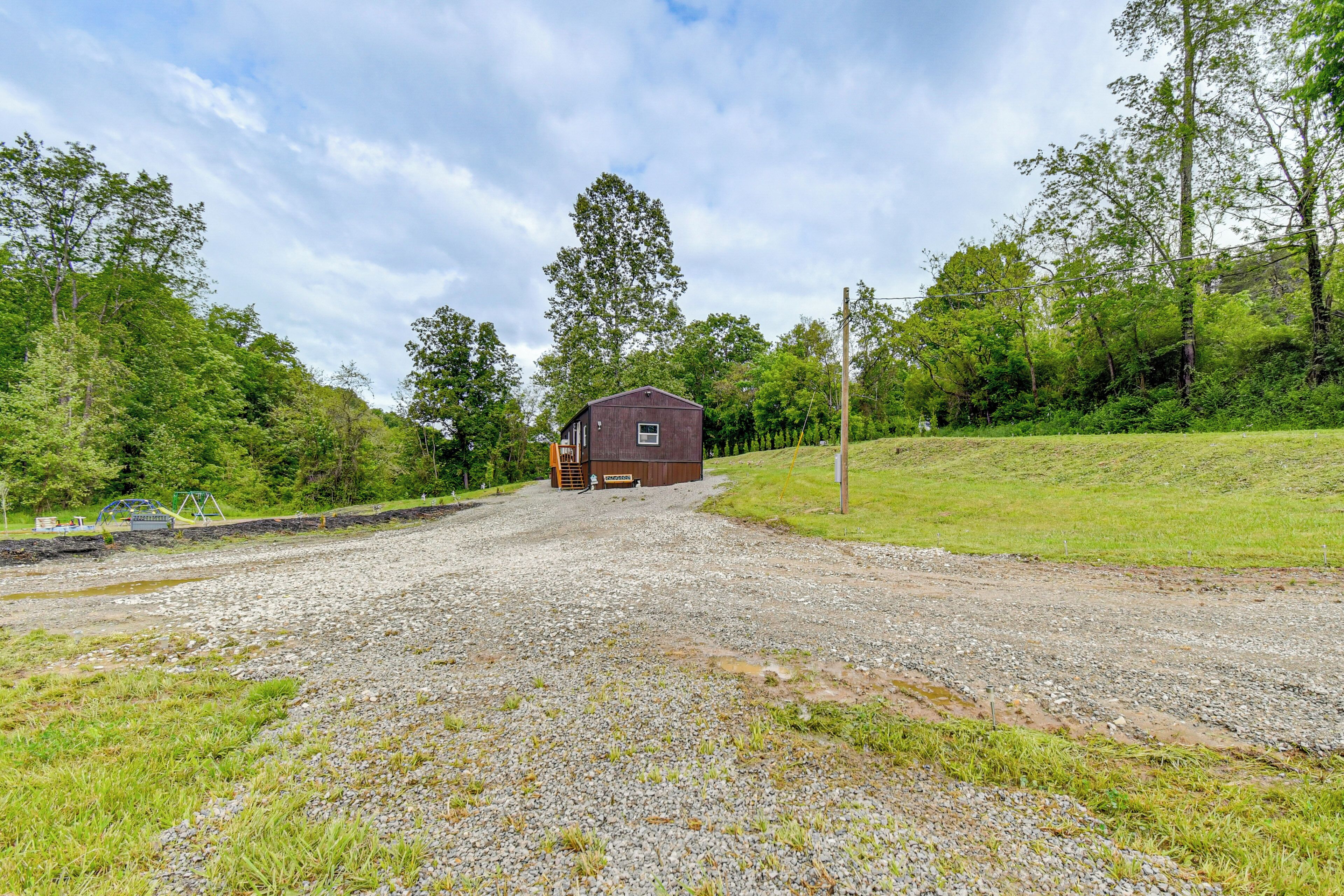 A gravel driveway leading to a wooden cabin surrounded by greenery.
