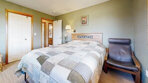 Een slaapkamer met een groot bed, een stoel, een nachtkastje en een lamp.