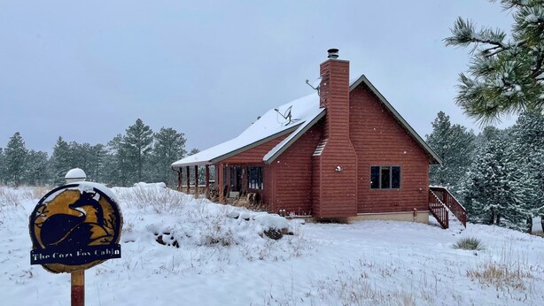 Een rode hut met een sneeuwbedekte dak en een schoorsteen, omgeven door sneeuw en bomen.