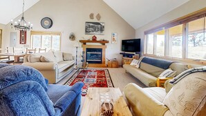 Een ruime woonkamer met een hoge plafond, een open haard, een televisie en comfortabele zitmogelijkheden.