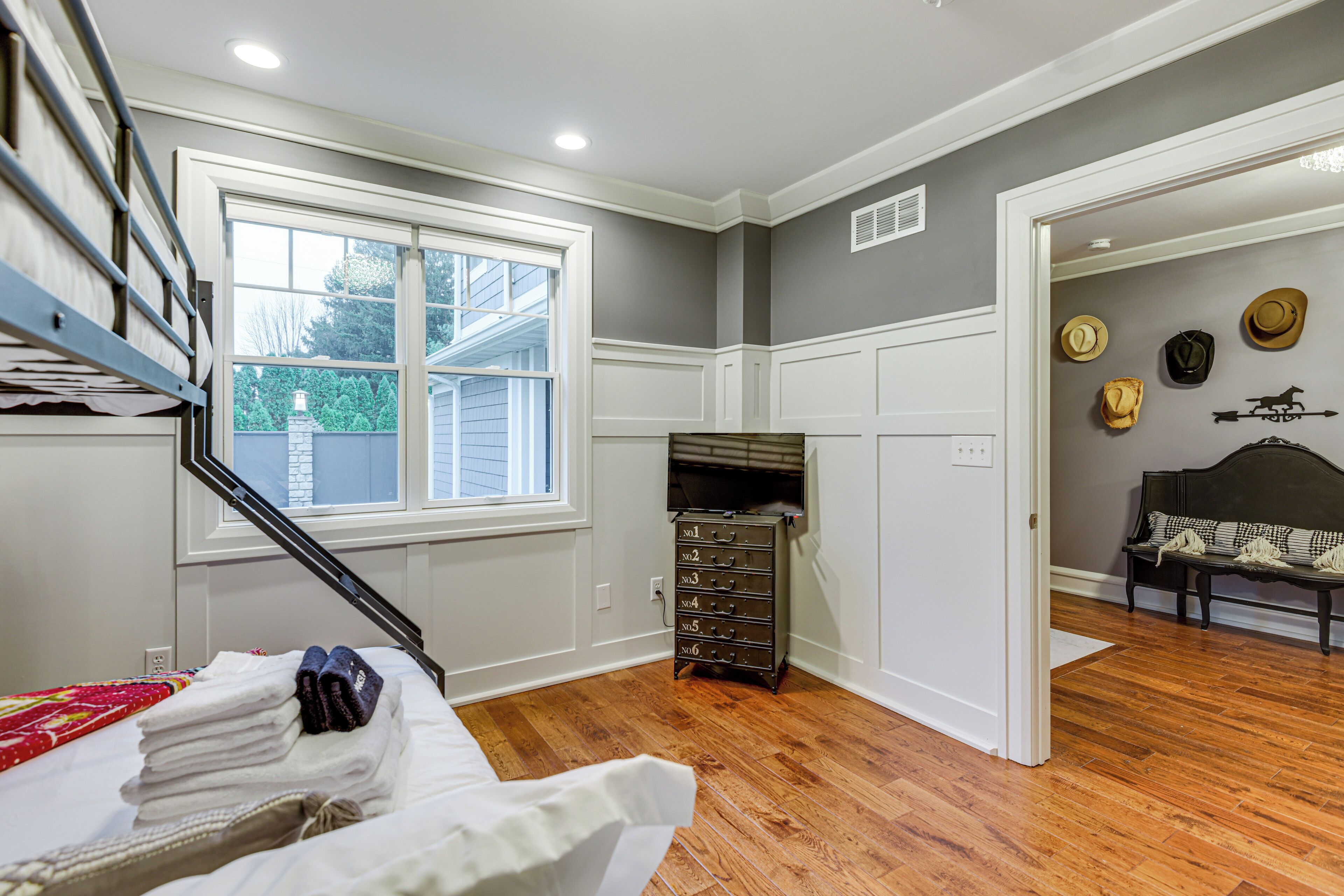 A bedroom with a bed, a dresser, a bench, and a wall with hats.