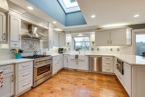 A modern kitchen with white cabinetry, a skylight, and a wood floor.