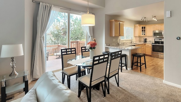 A modern kitchen with wooden cabinets, a stainless steel oven, and a dining area with a glass table and chairs. - Littleton Home w/ Deck - 24 Mi to Denver! (Littleton)