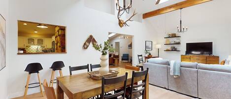 A spacious living area with a wooden dining table, chairs, a sofa, and a television.