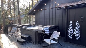 A hot tub on a wooden deck with chairs, string lights, and a garage door with leaf decals. - Hot Tub & Game Room! Pinetop 'wild Horse Retreat' (Pinetop)