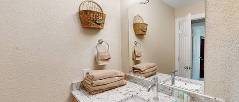 A bathroom with a marble sink, two wicker baskets, and a mirror reflecting the room.