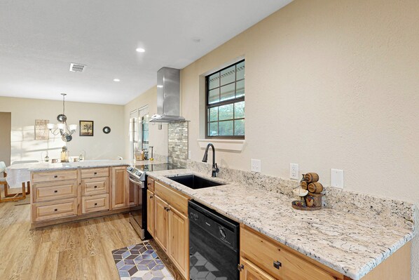 A kitchen with wooden cabinets, a granite countertop, a dishwasher, and a window.