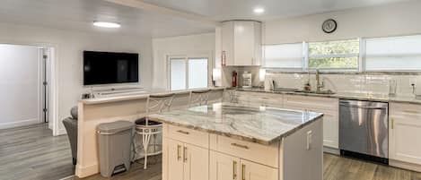 A modern kitchen with a marble countertop, stainless steel appliances, and a flat-screen TV mounted above the island.
