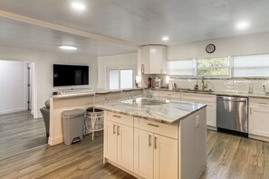 Una cocina moderna con encimera de mármol, electrodomésticos de acero inoxidable y un televisor de pantalla plana sobre la isla.