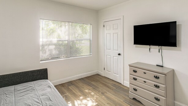 A bedroom with a bed, a dresser, a television, and a window with blinds. - 3BR Charming Retreat W & Deck & Wifi (Valdosta)