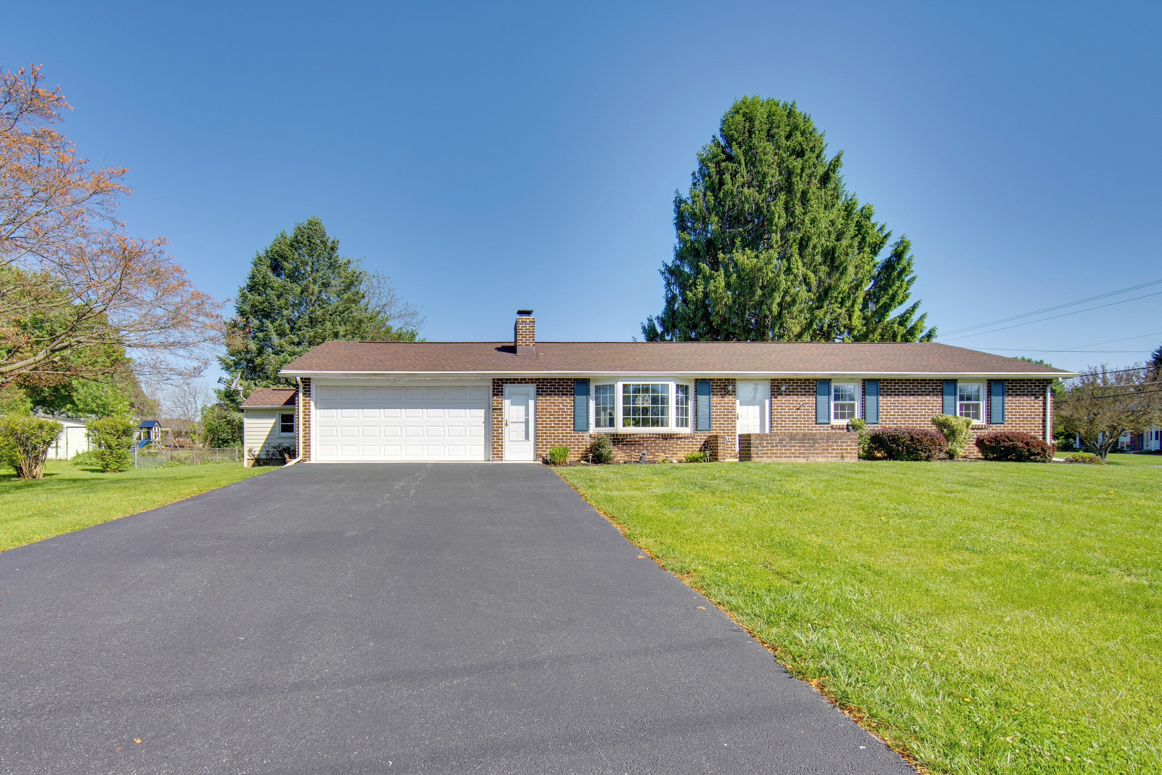 A single-story house with a garage, a front lawn, and a large tree.